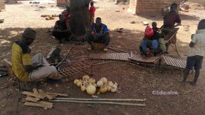 Au Burkina Faso, des villageois sont assis parterre et fabriquent des balafons. On voit à côté d'elles des calebasses vides et des planchettes de bois prêtes à être utilisées. 